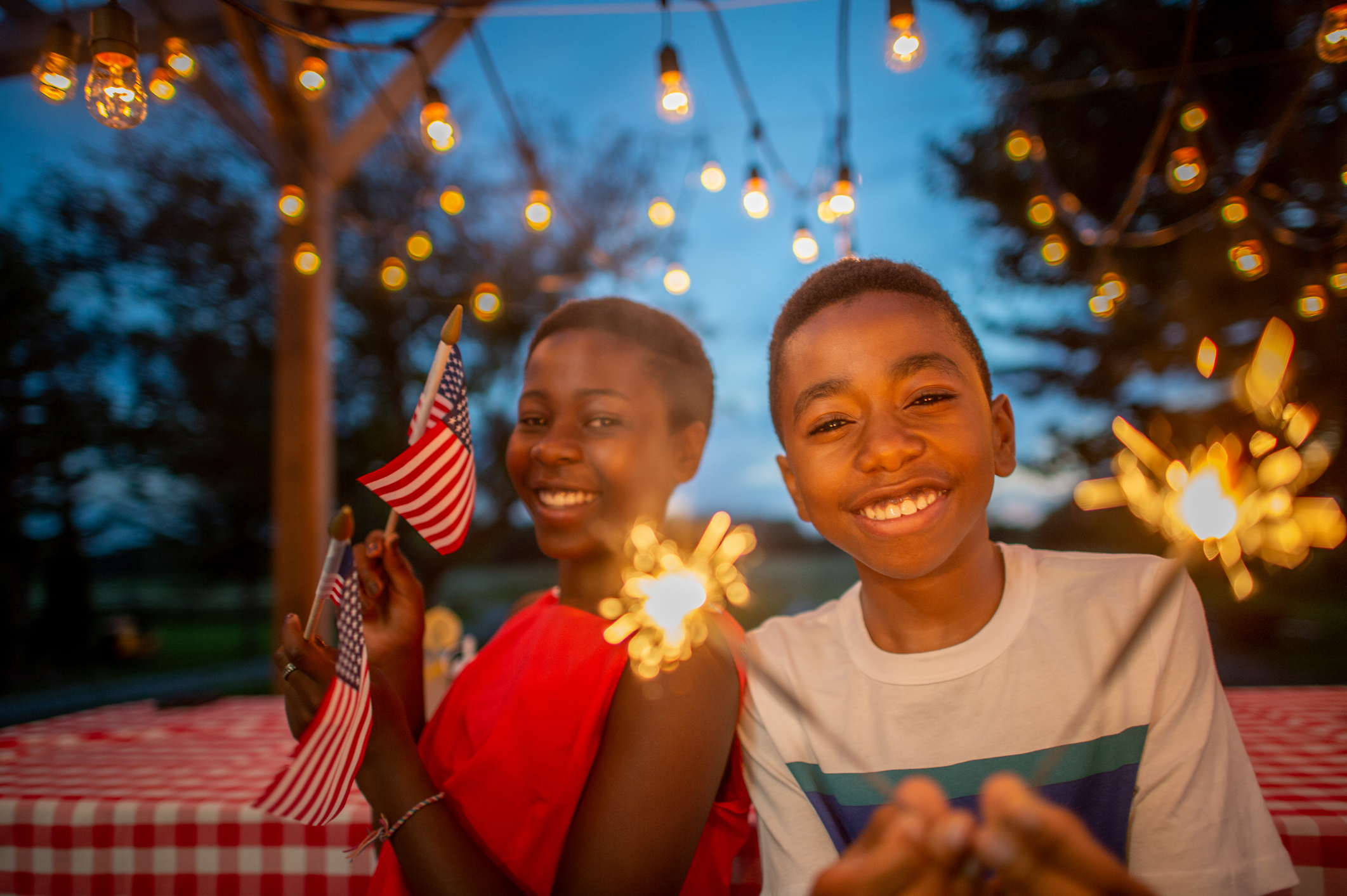 Celebrating 4th of July in Sussex County, NJ. Two African American children smile waving American flags and playing with sparklers.